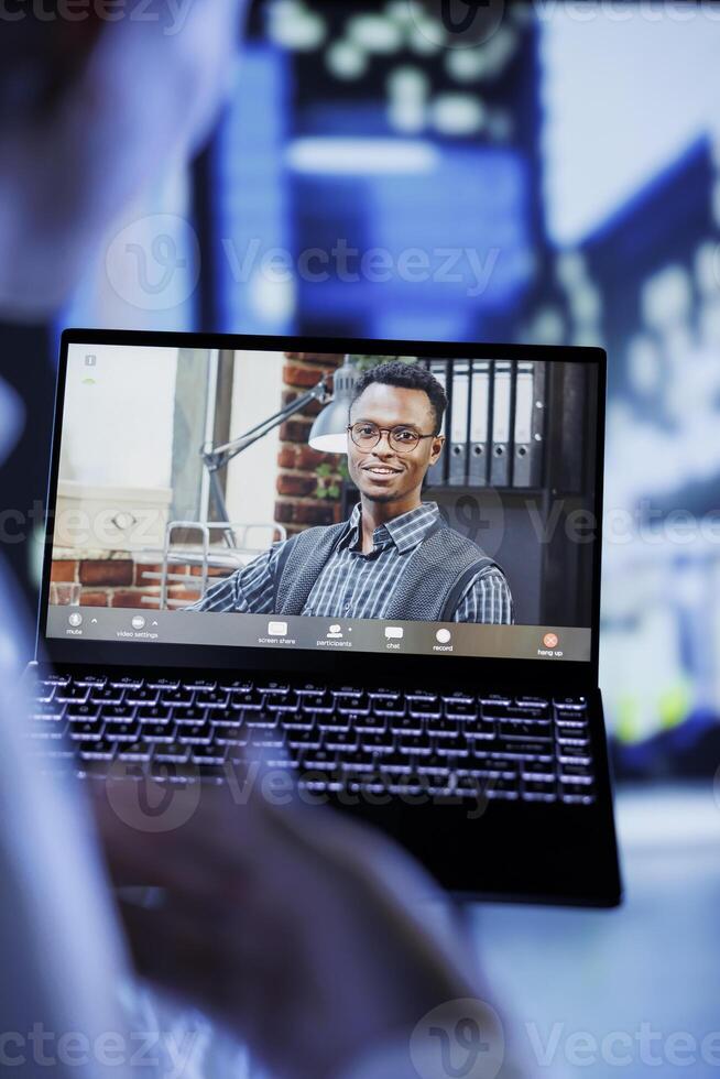 Close up of man in videocall with coworker while strolling around city streets at night, giving him work updates. Person uses laptop to show colleague urban surroundings in blurry background photo