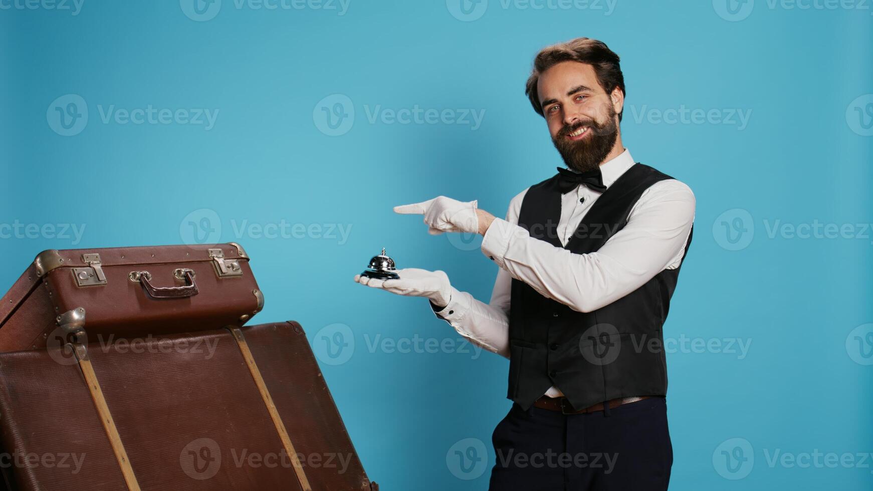 Male employee points at service bell, representing hotel concierge assistance and ringing for help with trolley bags. Formal skilled doorman assisting with travelling luggage, tourism sector. photo