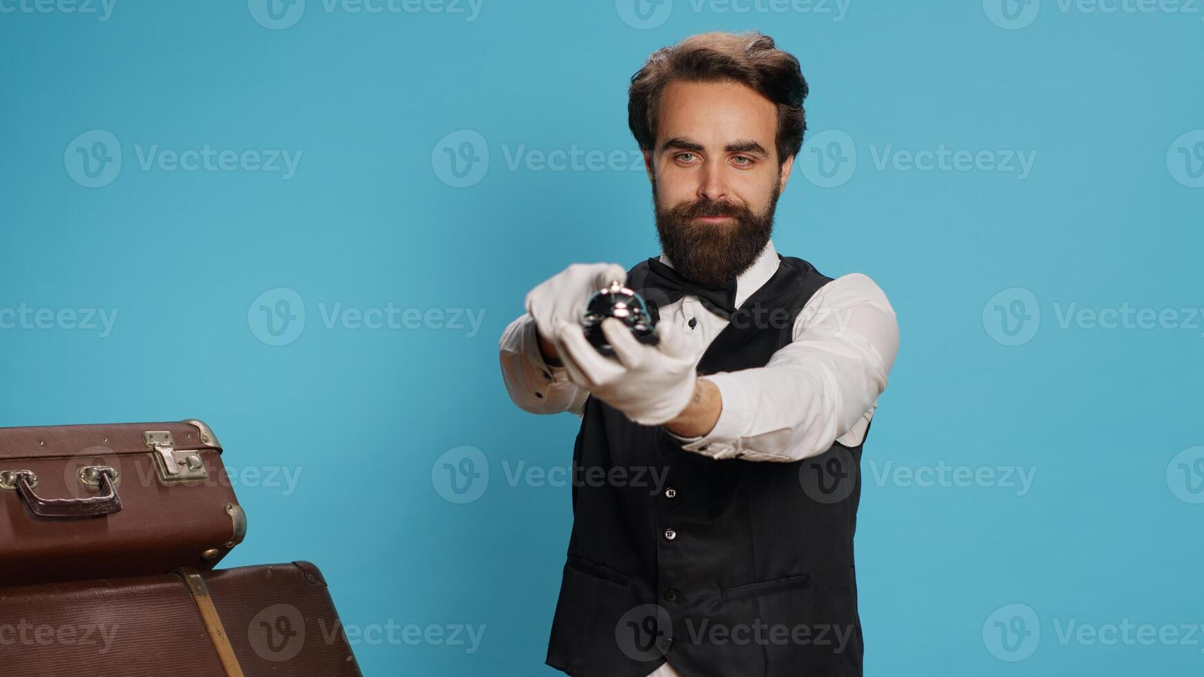 Doorkeeper with briefcases and bell, using to ring for hospitality service or assistance at hotel. Young bellhop employee ready to help people, working in tourism industry with confidence. photo