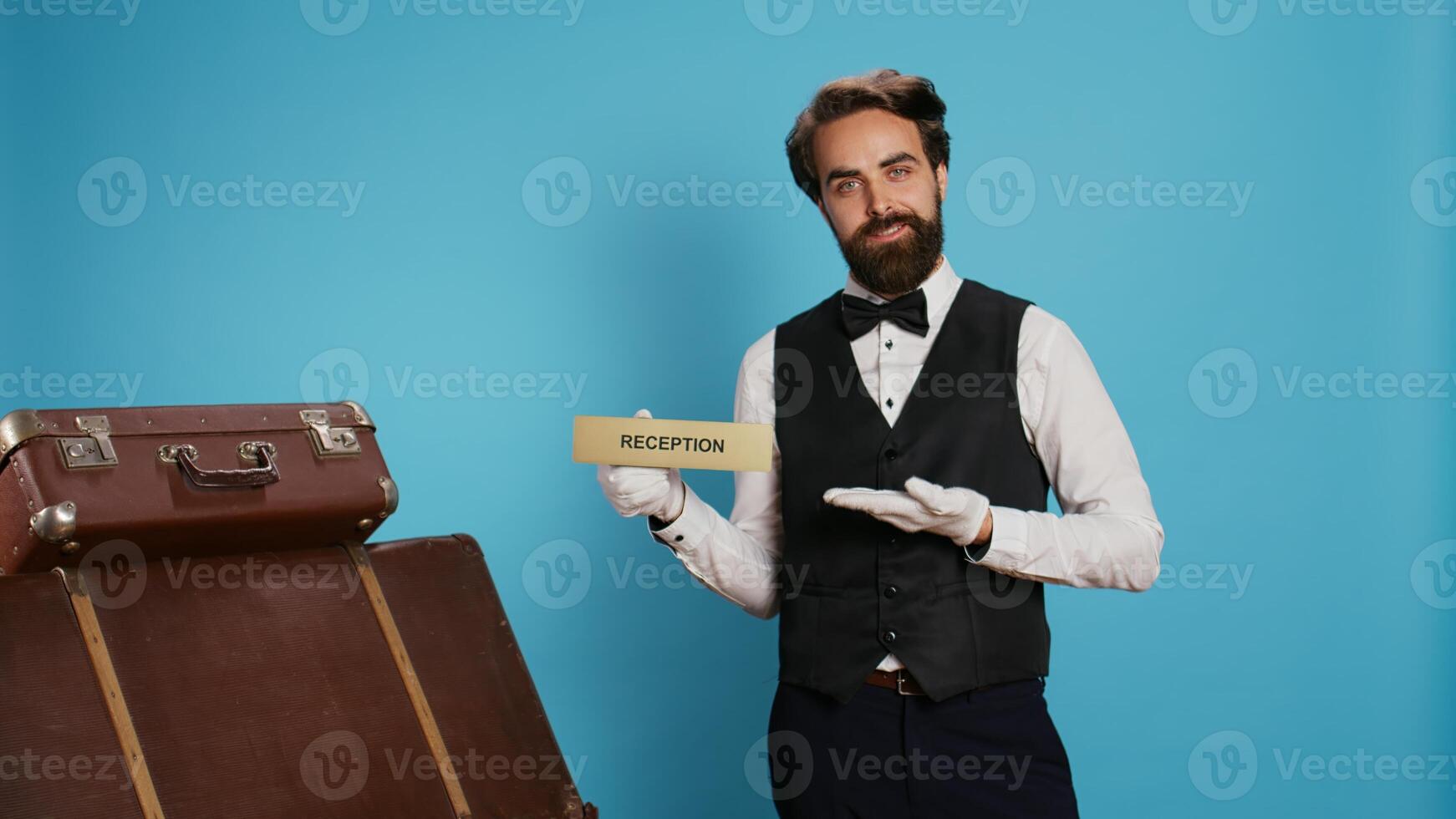 Hotel staff shows reception pointer on camera, leading guests in the right direction or area. Professional luxury doorman working in tourism travelling sector, showing front desk indicator. photo