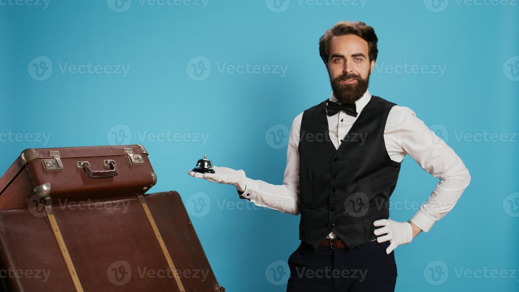 Hotel concierge shows service bell ringing for assistance, showcasing tourism and hospitality industry concept. Male porter helping with suitcase pile, luxury experienced doorman. photo