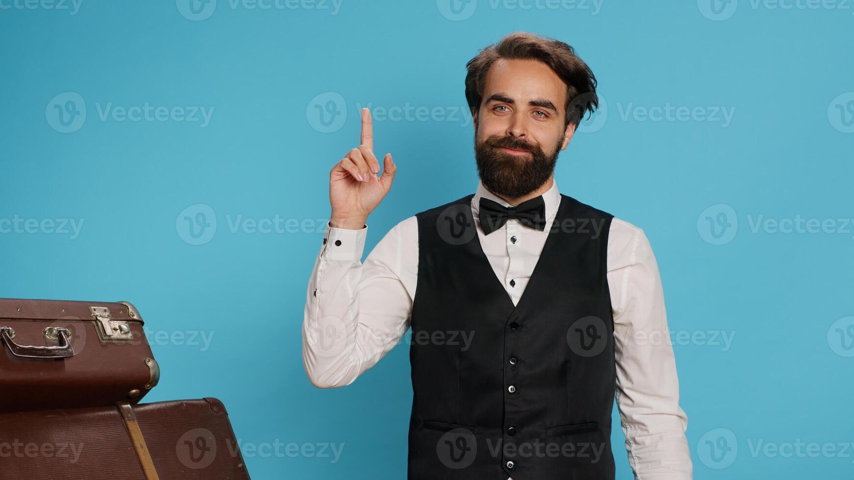 Hotel porter coming up with idea, looking for solution on camera against background. Formal luxury employee in suit acting like a genius and thinking about new answer to solve problem. photo