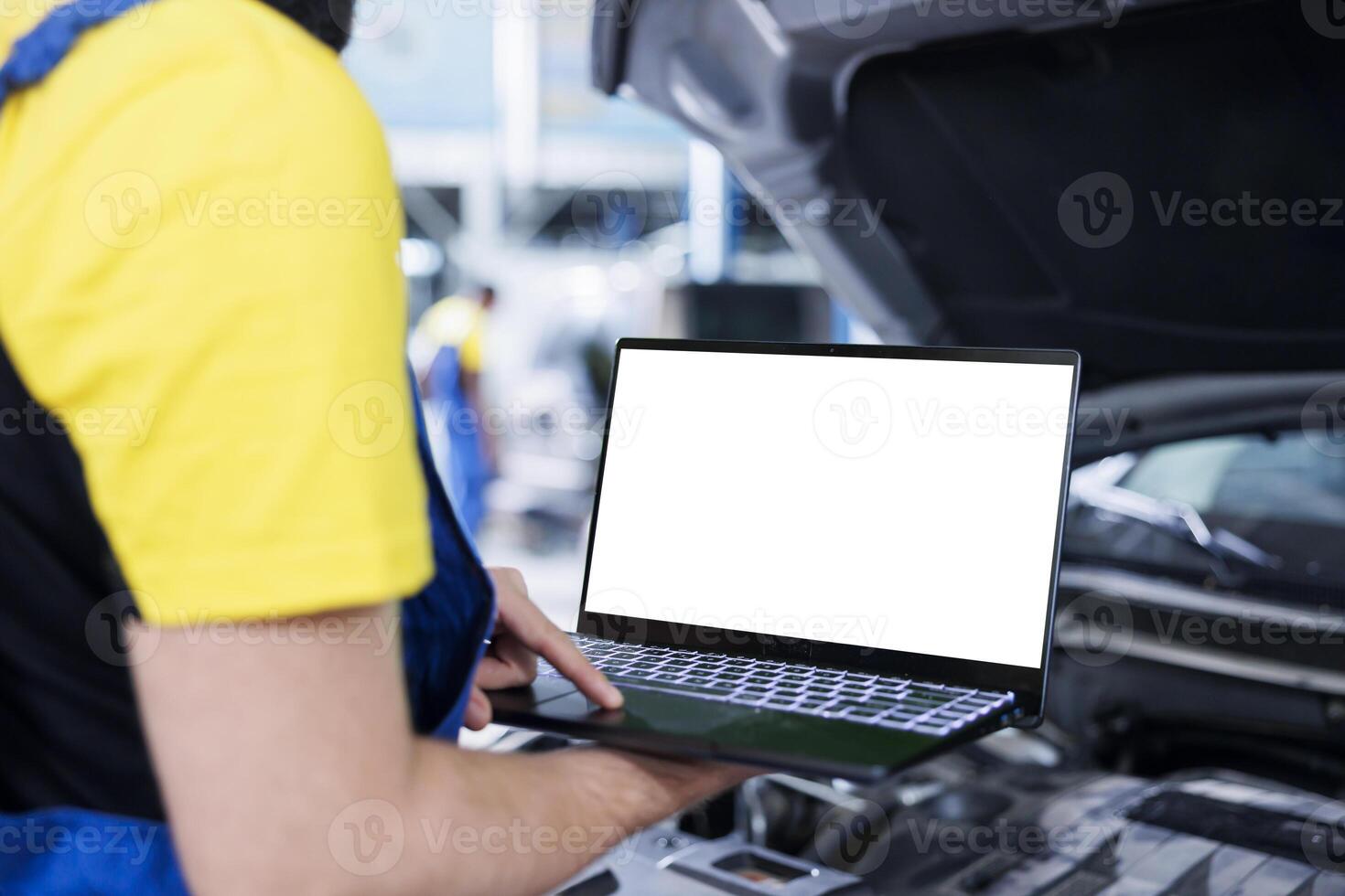 Seasoned mechanic in garage using mockup laptop to follow checklist while doing maintenance on car. Employee in auto repair shop does checkup on vehicle helped by isolated screen device photo