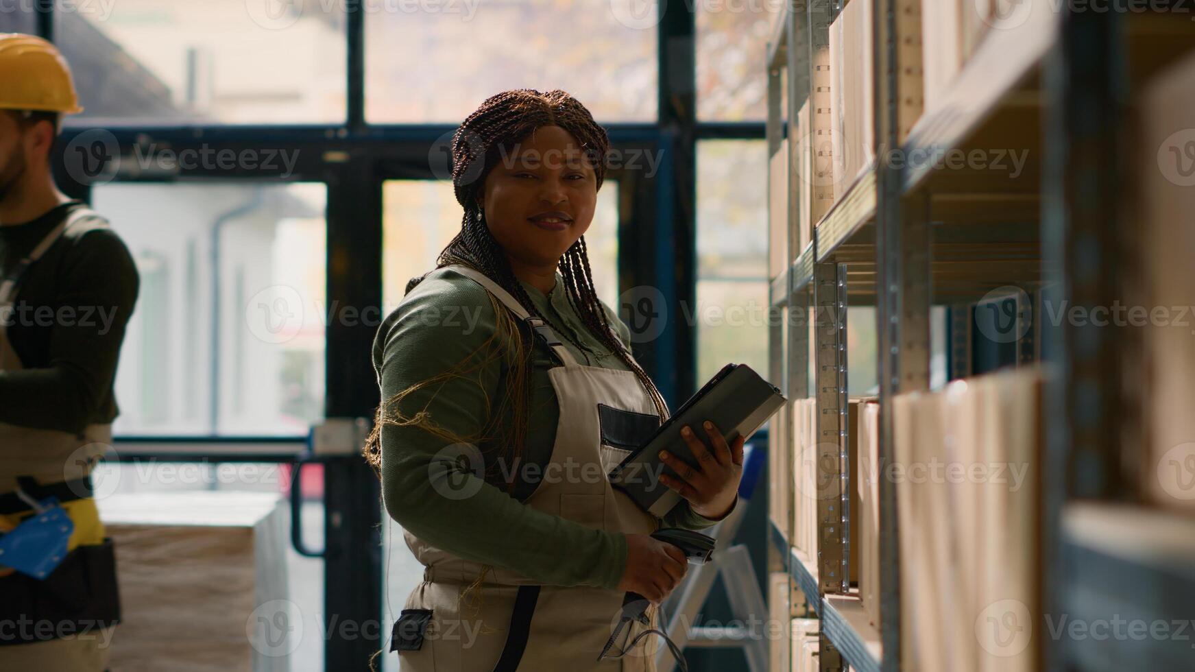 Portrait of african american head of logistics in warehouse, scanning items and updating prices for online ecommerce website while trainee in background handles cardboard boxes ready to be shipped photo