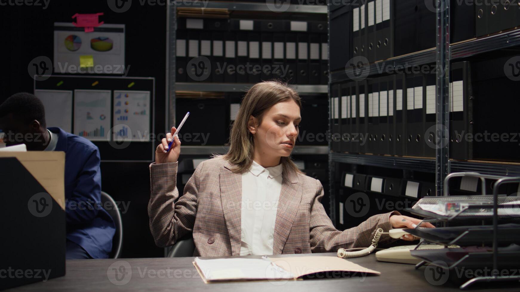 On landline phone, female law enforcement official gets critical information and gives african american policeman fresh case leads. In incident room, caucasian private investigator on telephone call. photo