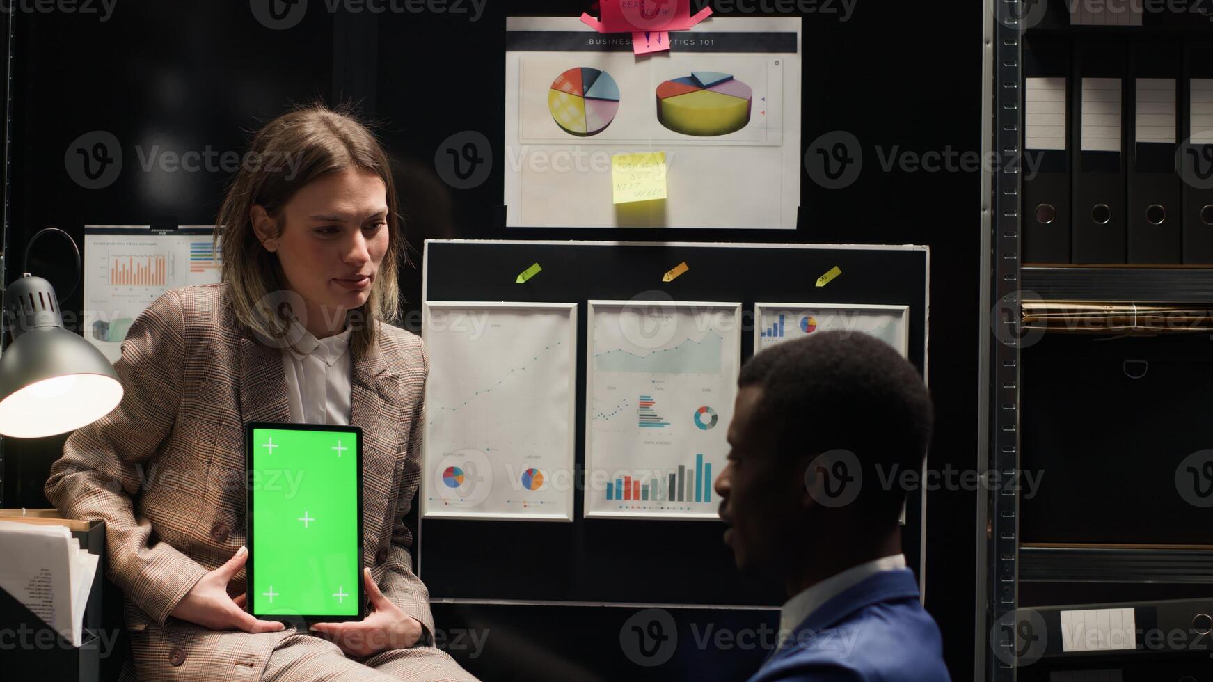 Female investigator grasps device with greenscreen to present mockup display, conducting criminal investigation. Male detective speaks with policewoman holding tablet with isolated copyspace template. photo