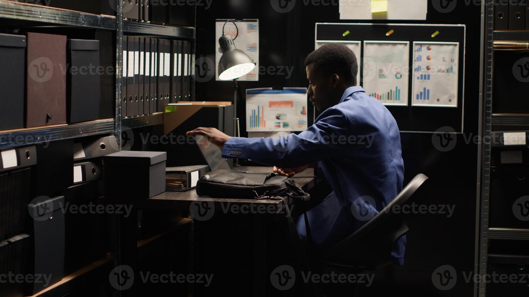 African American detective inspector arrives at office, investigating crime. Clues, evidence, files, photos, and records fill the room. Laptop bag indicates reliance on technology. photo
