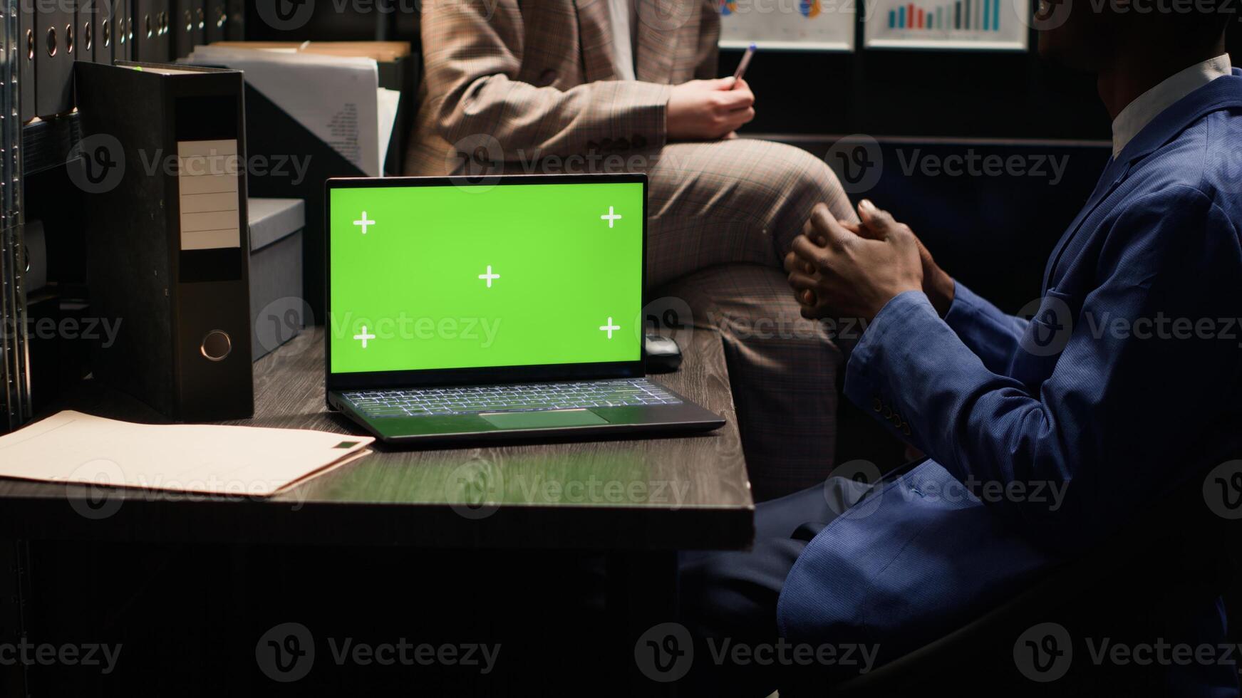Modern laptop with blank green screen positioned on desk in police evidence room. In the office, wireless computer displays isolated chromakey copyspace template while officers talk in background. photo
