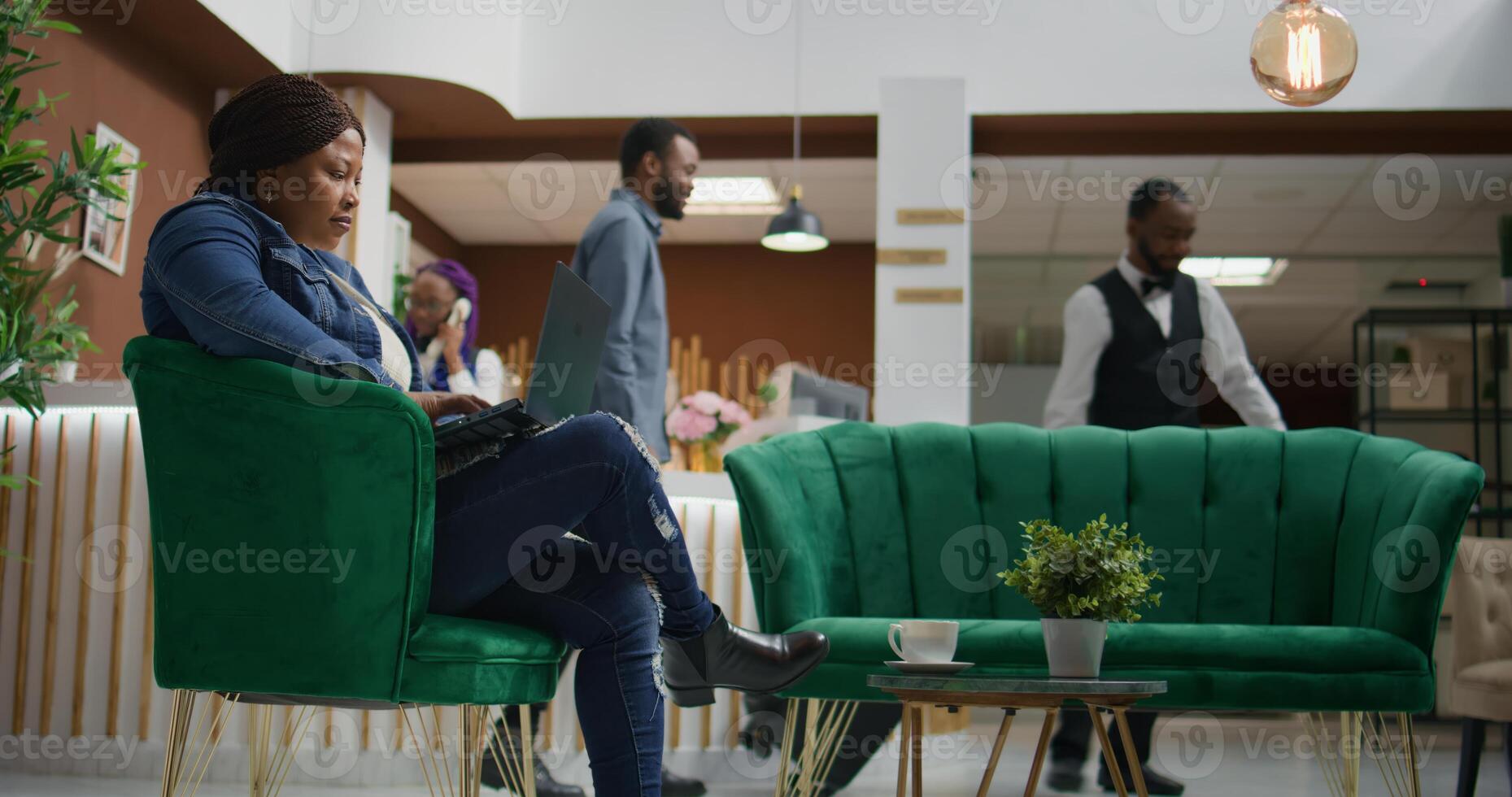 Hotel guest verifying webpage at hotel, waiting for accommodation at holiday resort. African american woman using laptop to review files and check social media before seeing room. photo
