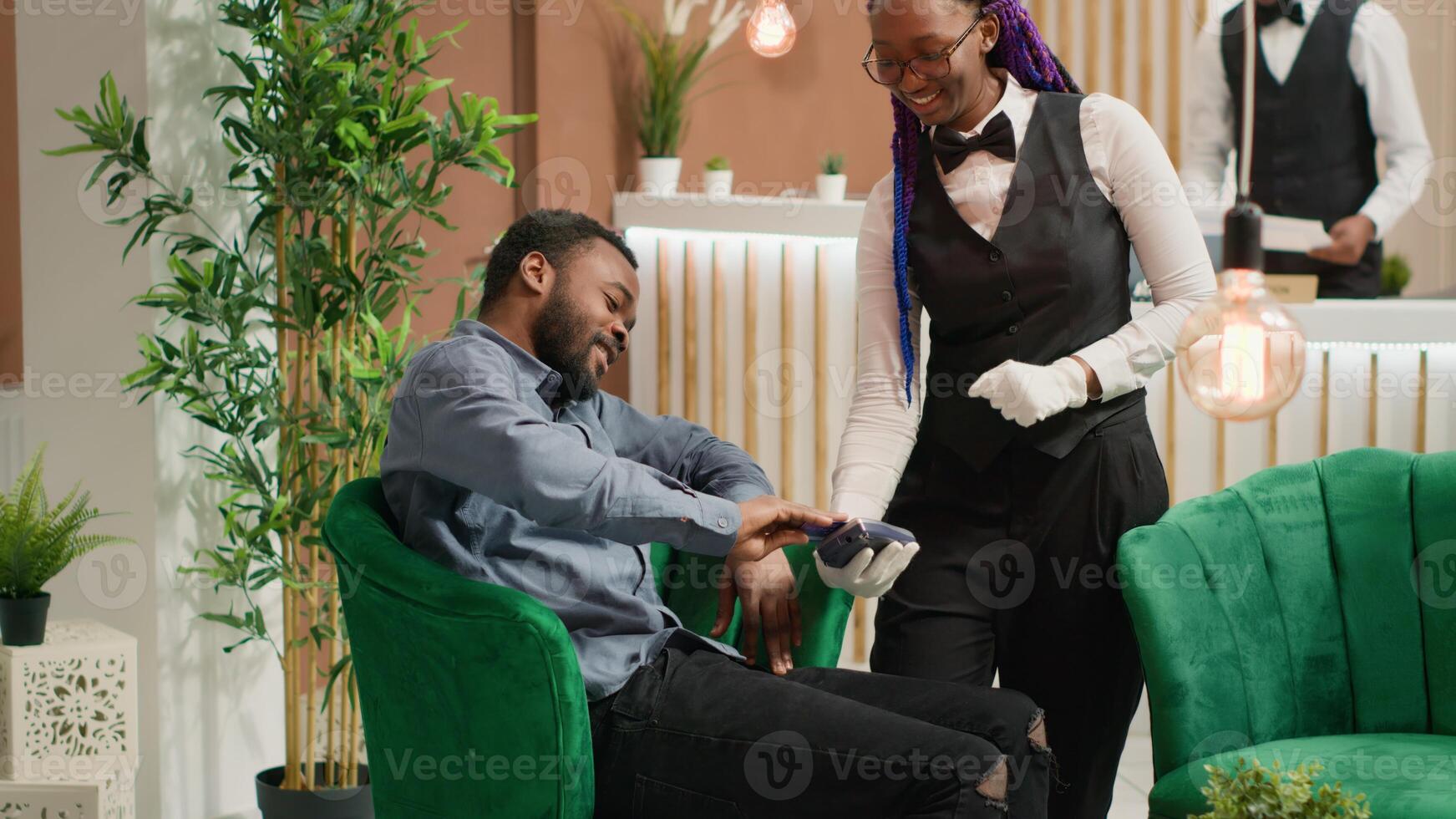 Guest paying for cup of coffee to hotel staff, using card at pos while he waits for room registration. African american traveller paying for drink, discussing with receptionist about services. photo