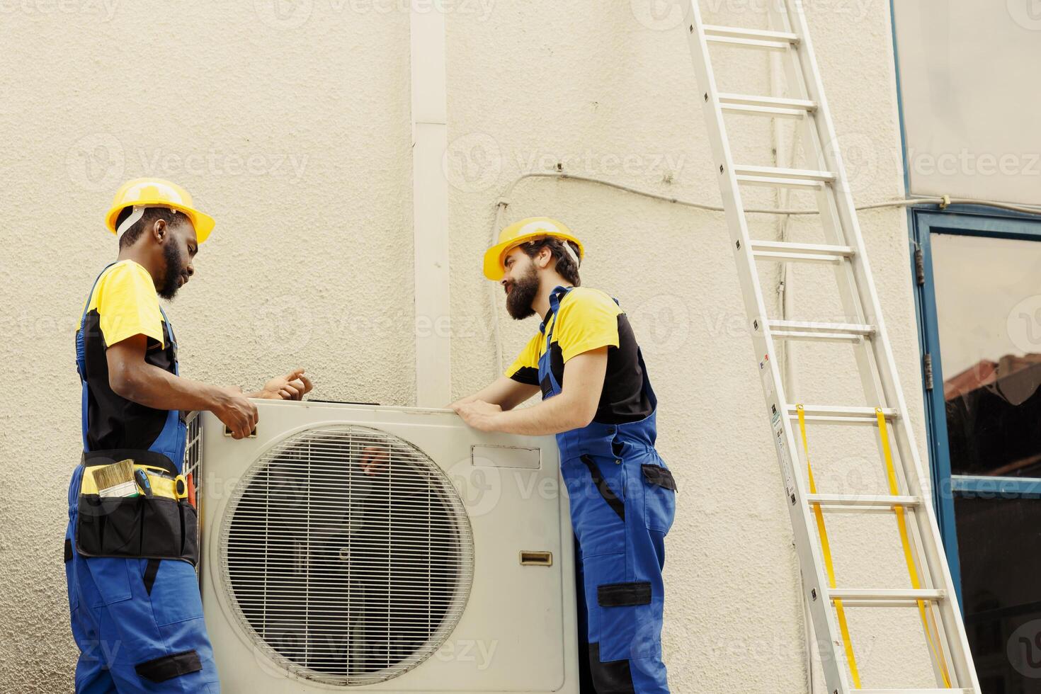 African american mechanic and apprentice repairman taking apart old damaged external hvac system to replace it with new performant air conditioner after draining refrigerant and replacing ductwork photo