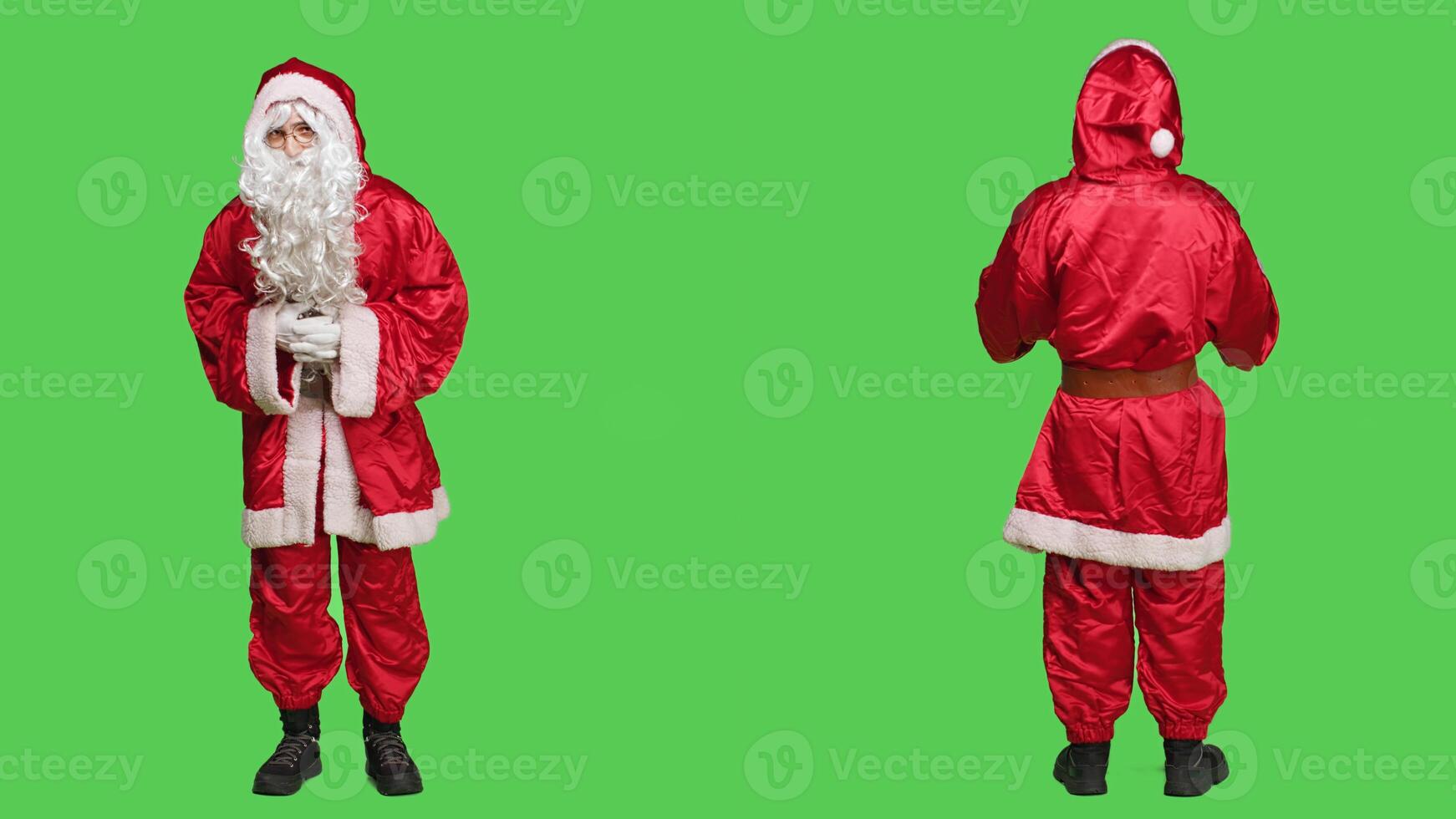 Santa claus on full body greenscreen backdrop, joyful person trying to spread christmas spirit with traditional festive costume. Saint nick with hat and beard, winter holiday celebration. photo
