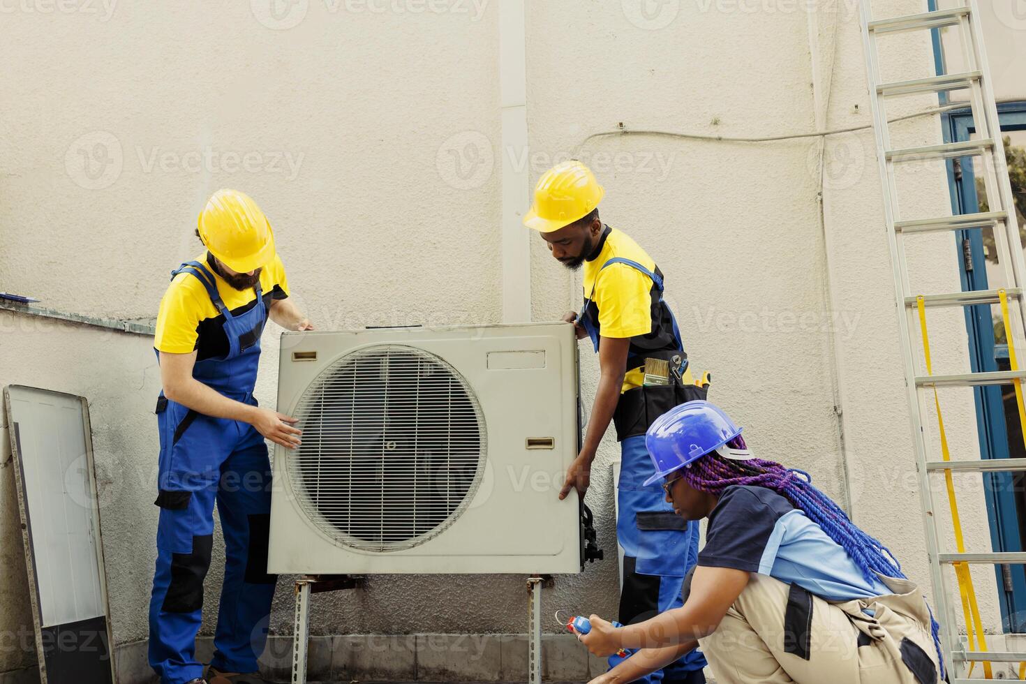 Proficient workers putting new external air conditioner in place for customer. Capable electrician with african american coworkers commissioned to optimize new HVAC system efficacy photo