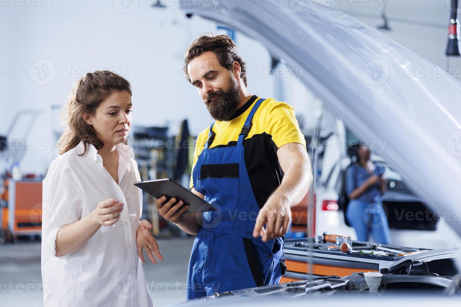 Technician at auto repair shop conducts annual vehicle checkup, informing client about needed engine replacement. Skillful garage worker talks with customer after finishing car inspection photo