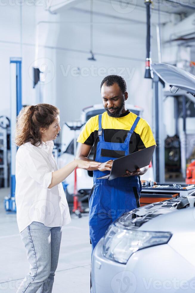 Mechanic in car service orders new fuel tank for damaged vehicle using laptop. Skilled technician next to customer looking online for components to replace old ones in malfunctioning automobile photo