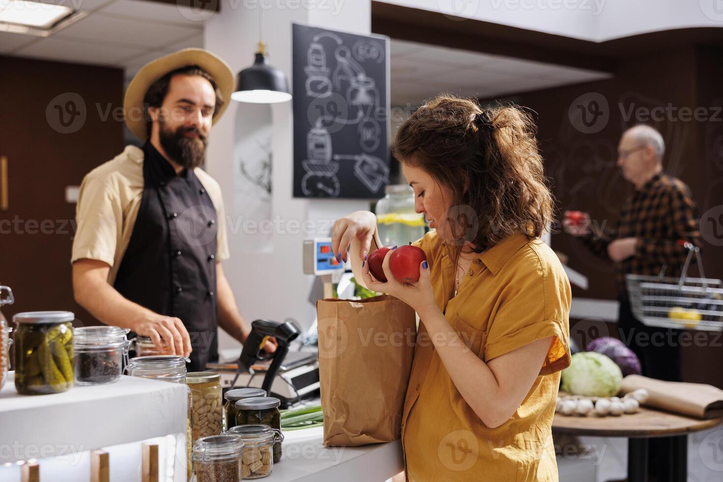 Woman at zero waste store checkout paying for chemicals free vegetables. Client in plastic free local grocery shop using decomposable paper bag to reduce environmental impact photo