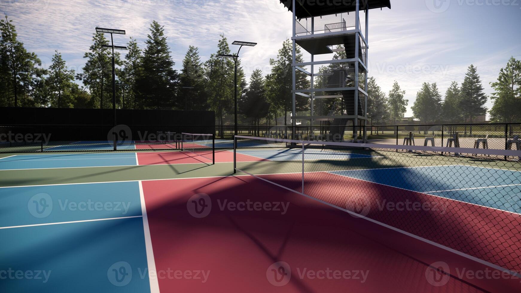 Empty pickleball courts with red, blue, and green floors marked by white lines, complete with lights, fencing, seating, and trees around the area photo