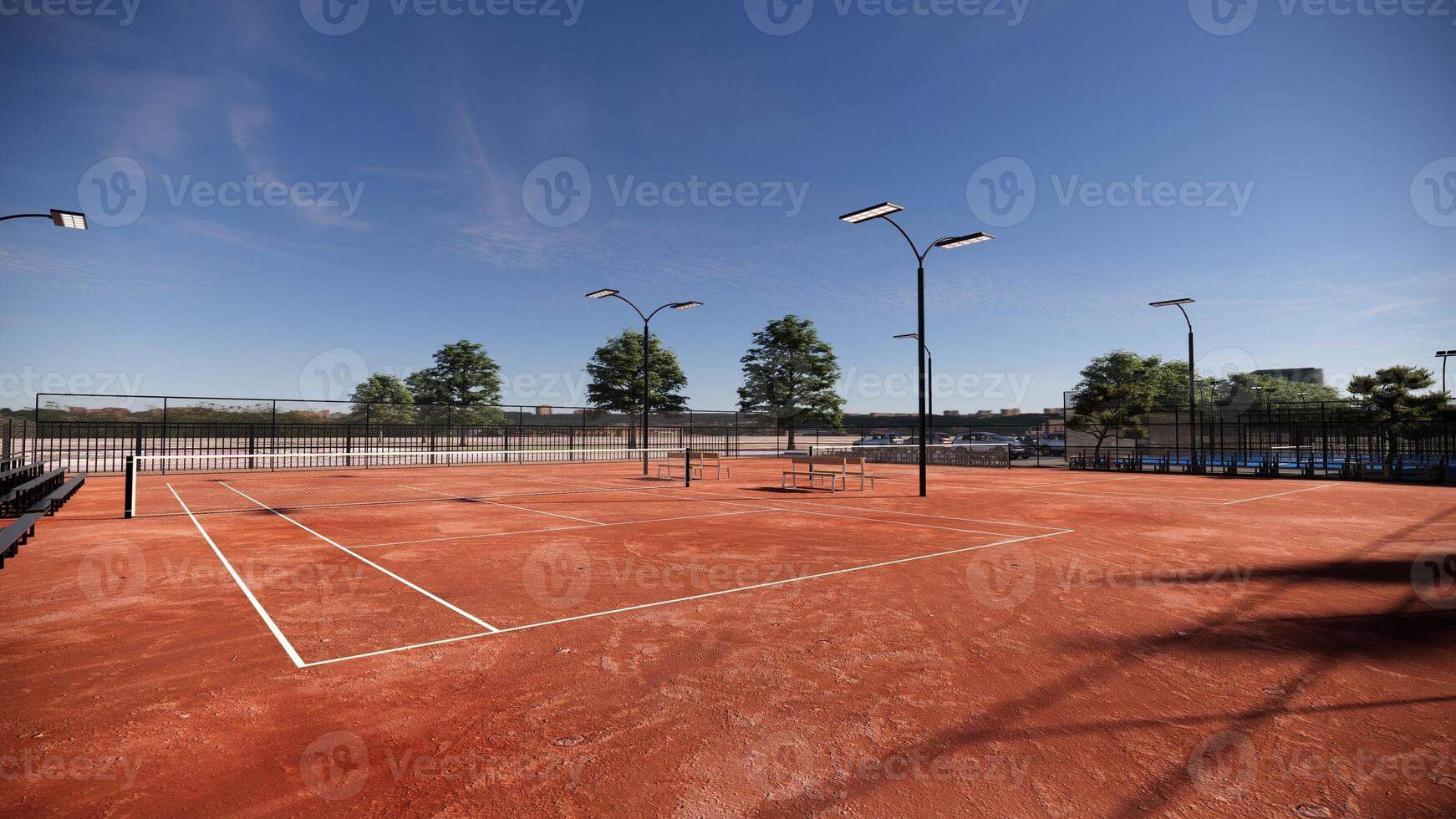outdoor tennis court adorned with a vibrant red clay surface, equipped with floodlights and lined with spectator benches photo