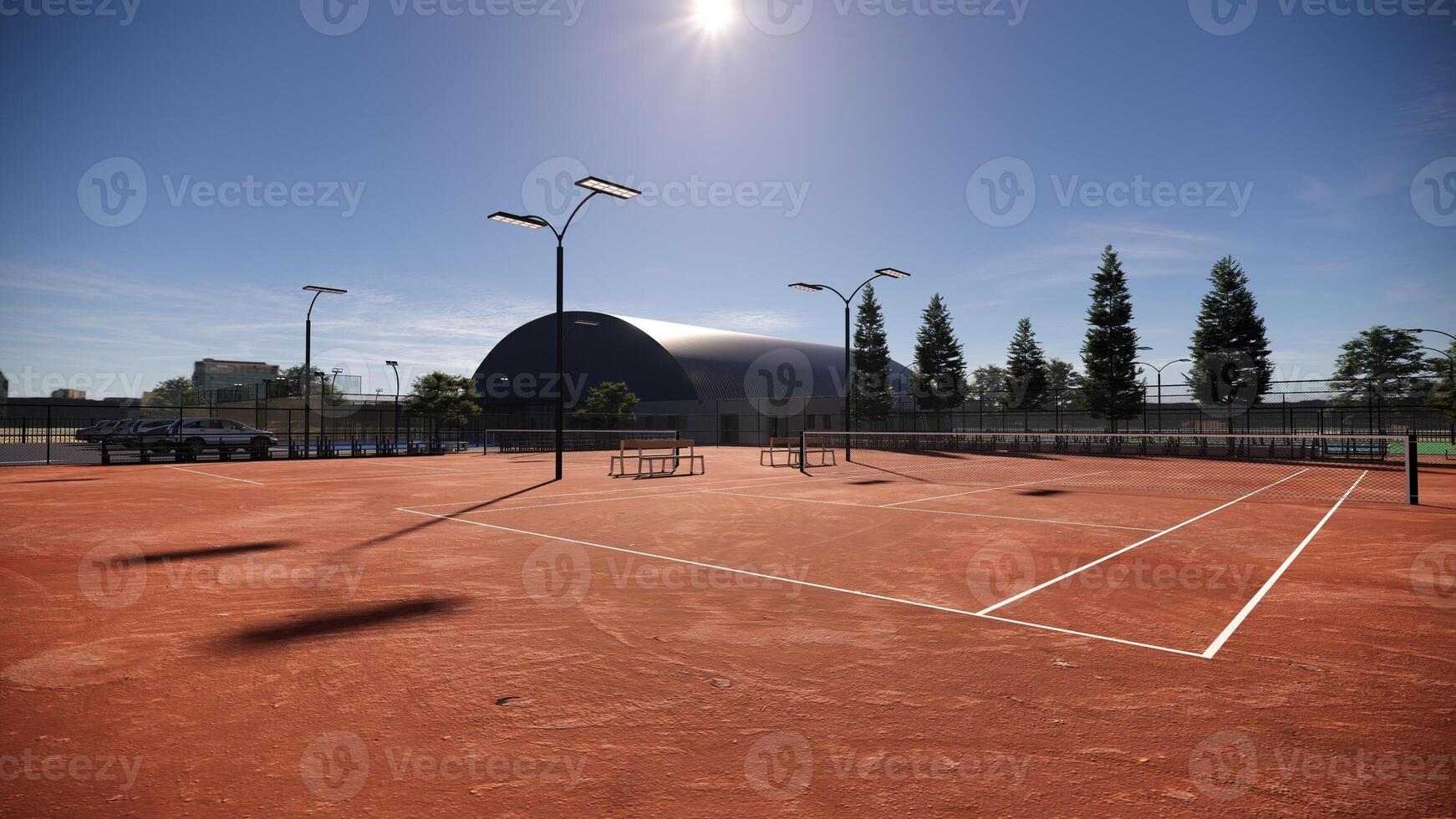 A sprawling red clay tennis court, illuminated by floodlights and flanked by spectator benches, invites exhilarating matches under the open sky photo