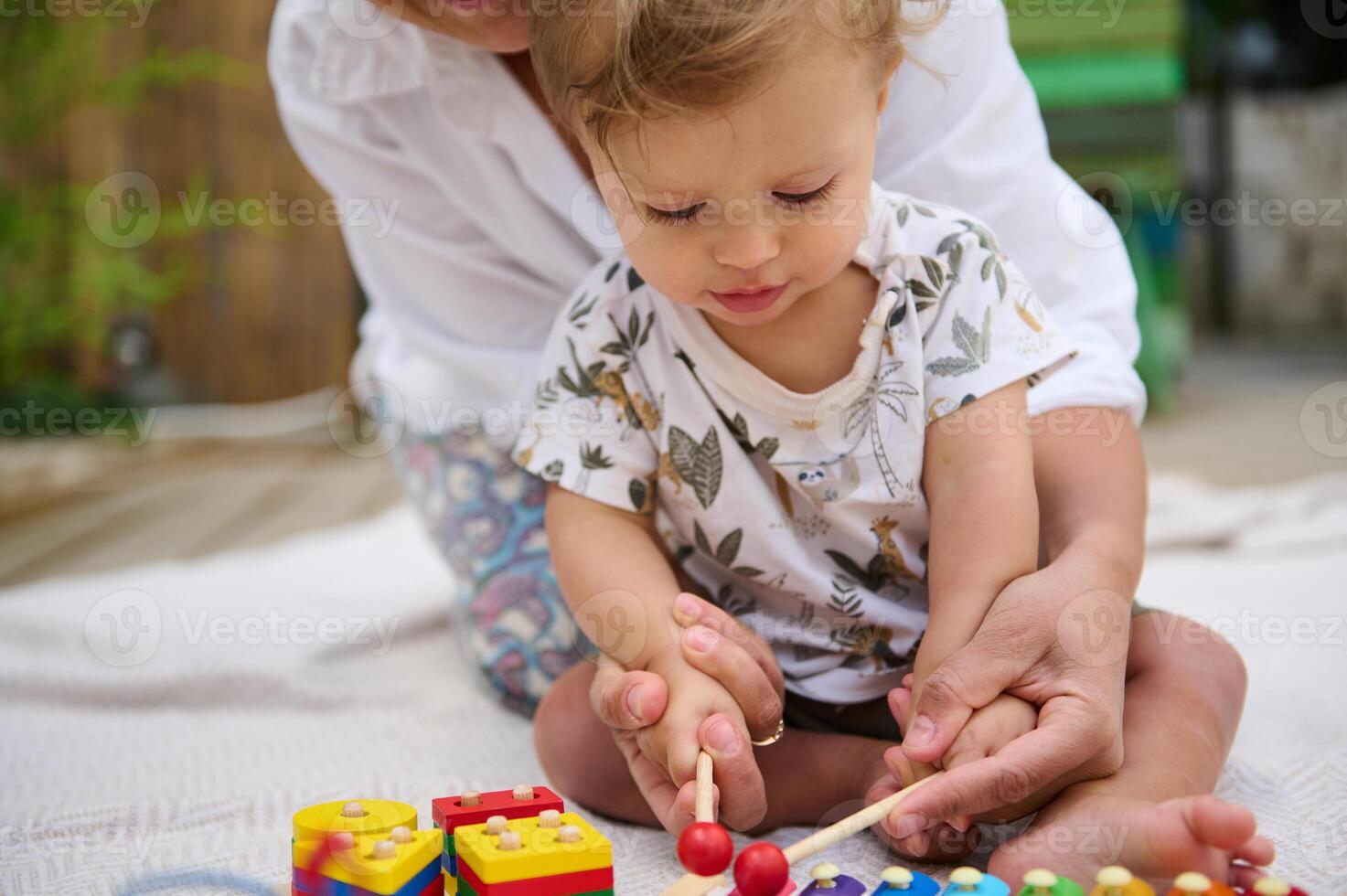 Toddler playing with xylophone assisted by parent outdoors photo