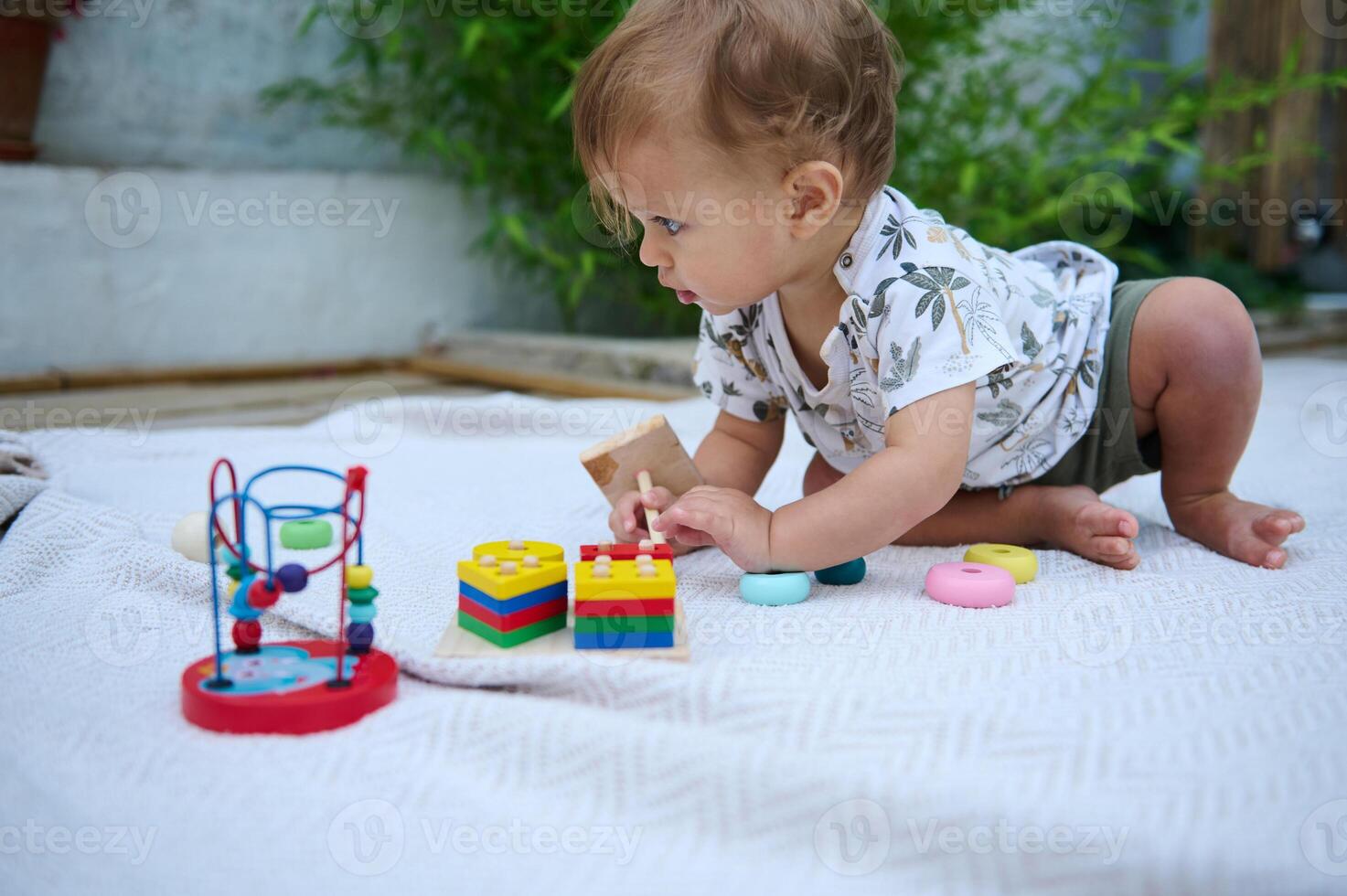Cute baby playing with colorful toys on a white blanket outdoors photo