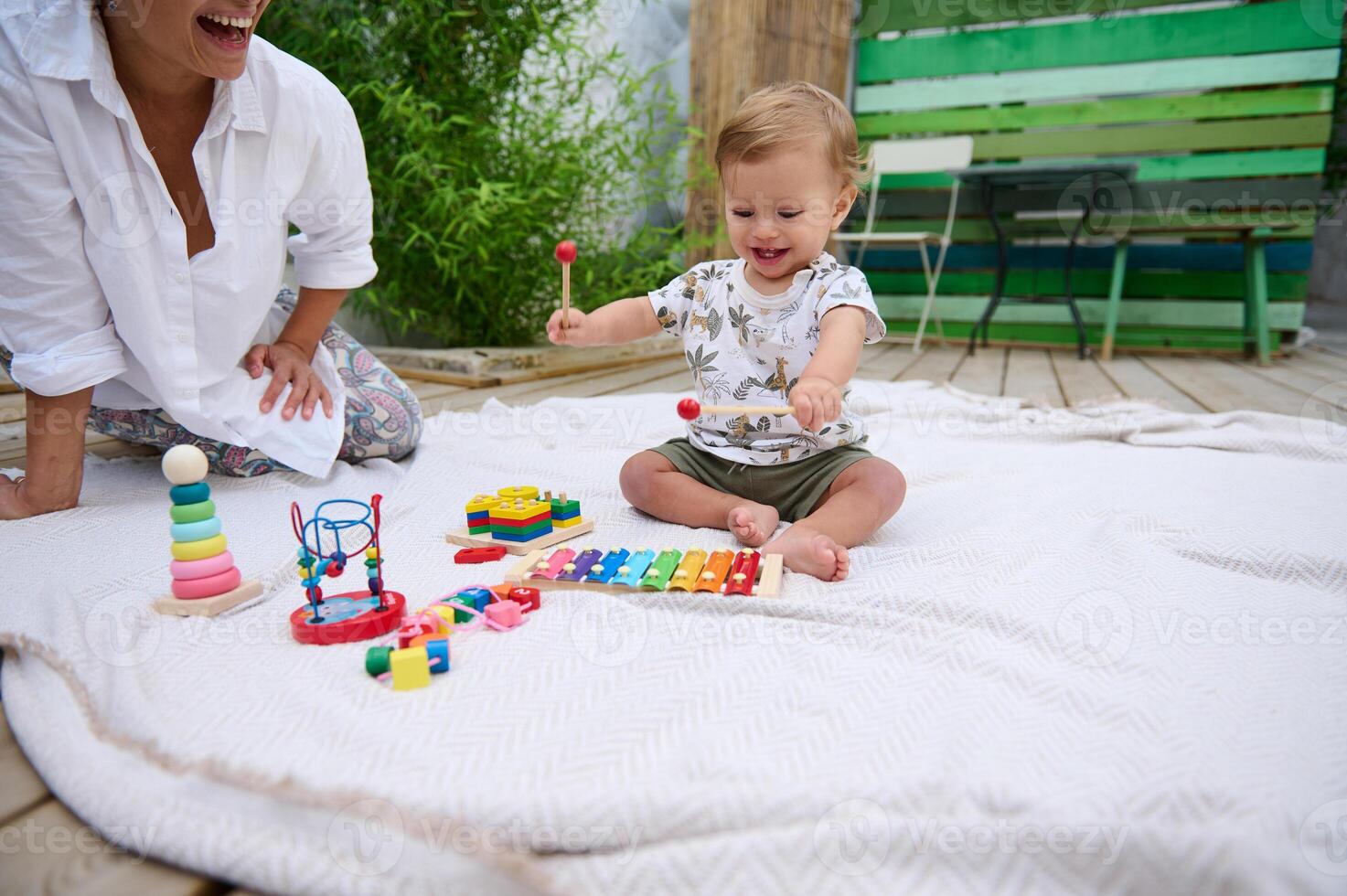 Smiling baby playing on blanket with colorful toys outdoors photo