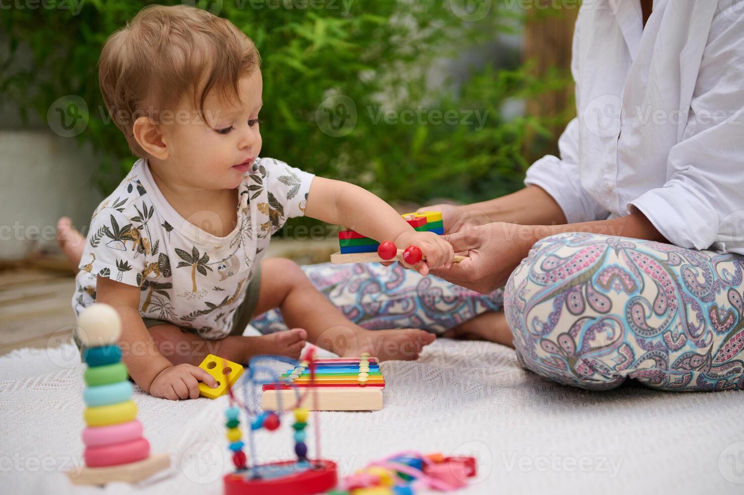 Baby playing with colorful toys on a blanket outside photo