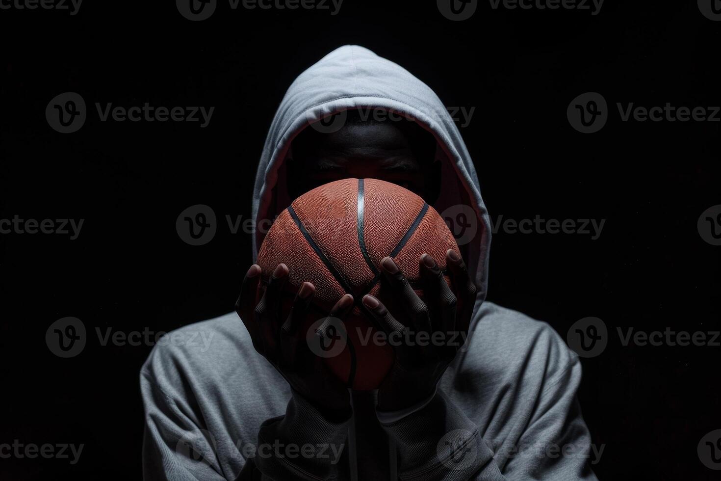 Mysterious figure in hoodie holding basketball, shadows and light playing across face emphasizing the sport's intensity and style. photo