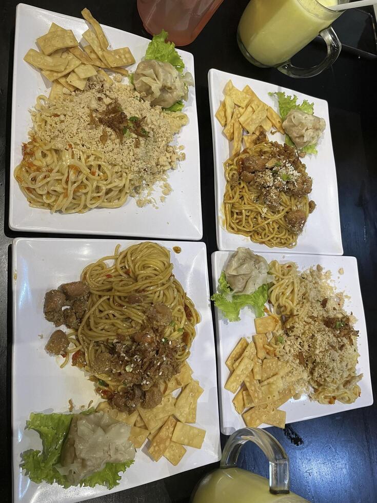 Indonesian food. noodles topped with chicken and dumplings. served on a square plate photo