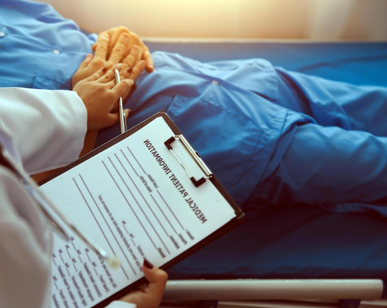 Hospitalized man lying in bed while doctor checking his pulse. Female physician examining male patient in hospital room. photo
