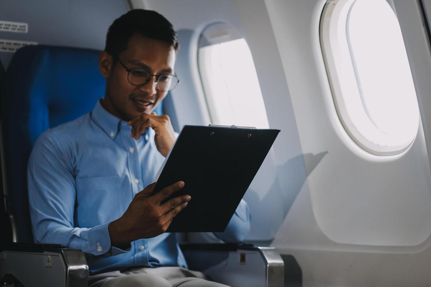 Attractive Asian male passenger of airplane sitting in comfortable seat while working laptop and tablet with mock up area using wireless connection. Travel in style, work with grace. photo
