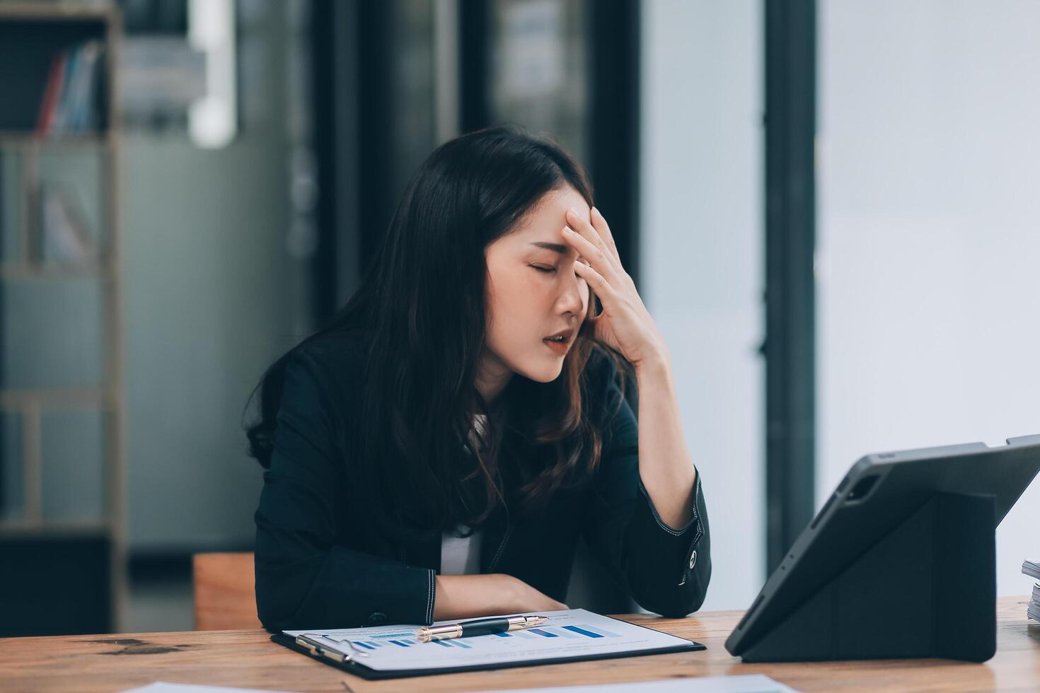 Young sad businesswoman is sitting at table, covering his face On desk is laptop, tablet computer, Stress. Serious woman concentrating on his paper work. photo