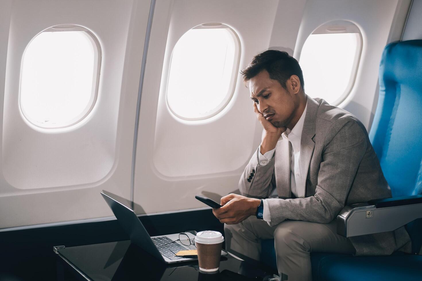 Stressed and professional Asian businessman in a business class, having a serious phone call with someone during the flight to a business meeting. photo