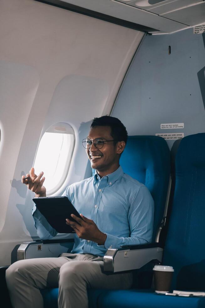 Attractive Asian male passenger of airplane sitting in comfortable seat while working laptop and tablet with mock up area using wireless connection. Travel in style, work with grace. photo