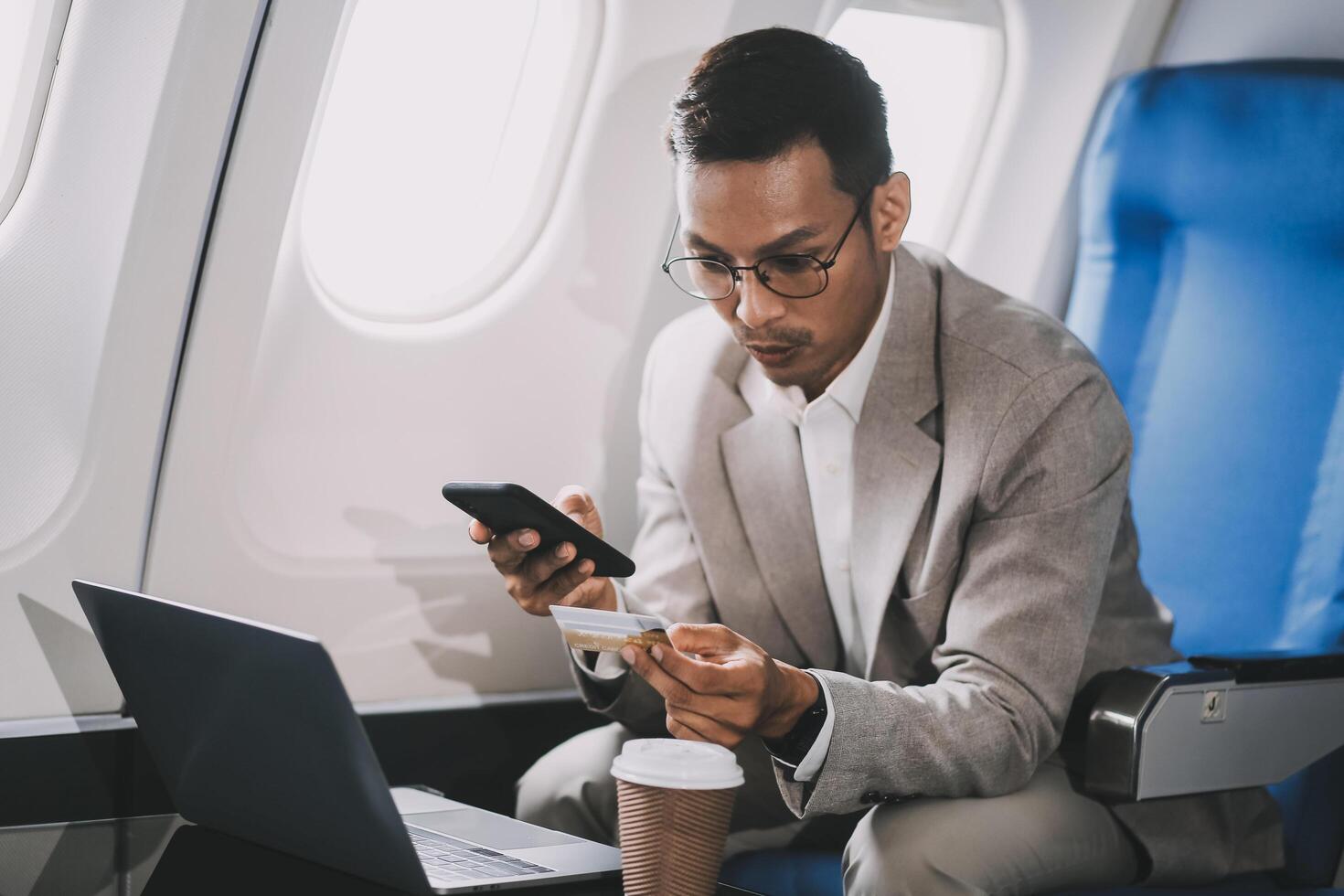 Businessman holding credit card and looking at camera near laptop in private jet photo