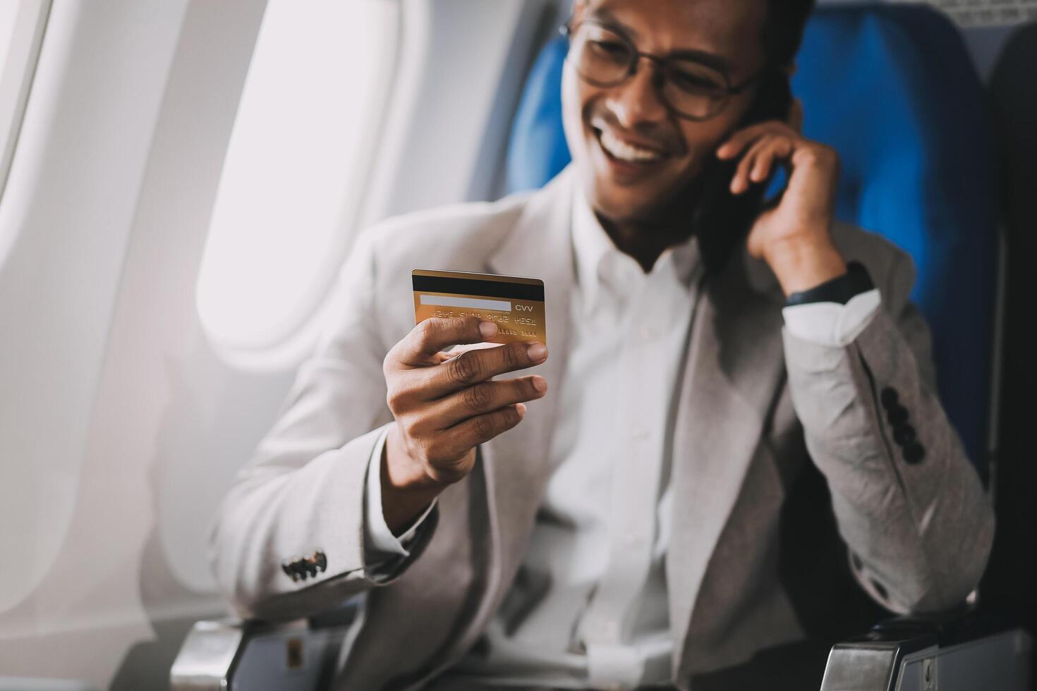 Businessman holding credit card and looking at camera near laptop in private jet photo