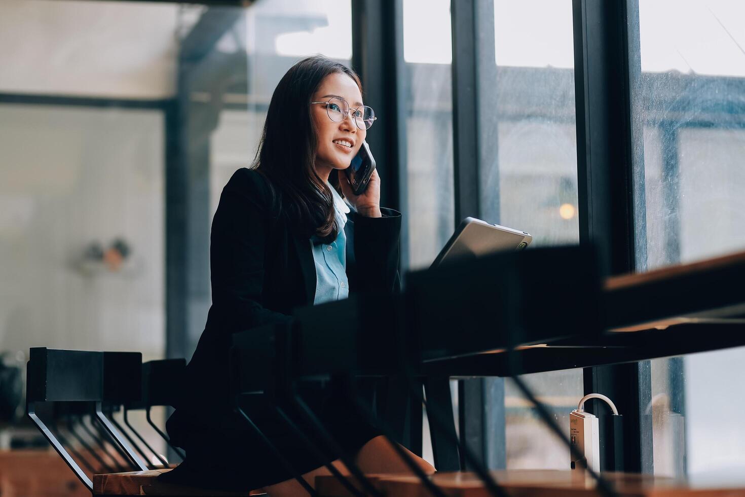 Asian woman entrepreneur busy with her work in the office. Young Asian woman talking over phone or cellphone while sitting at her desk. photo