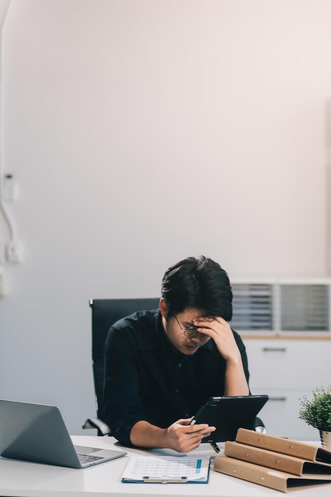 Frustrated Asian young businessman worker working on table in office. Busy employee worker people feel tired and headache from late work and overwork job document on computer desk at company workplace photo