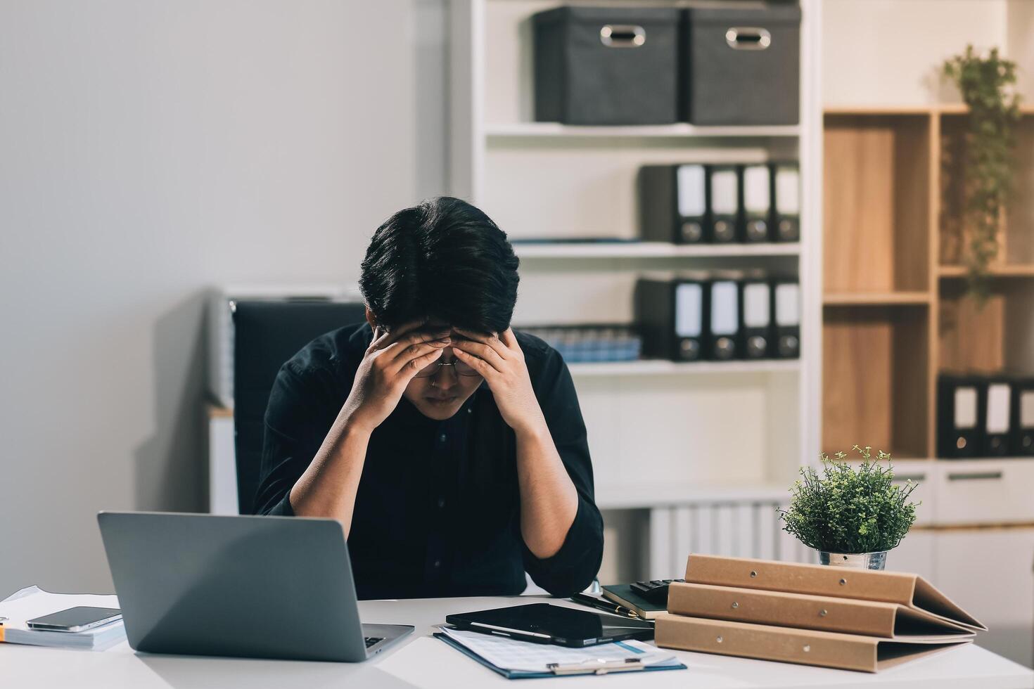 Frustrated Asian young businessman worker working on table in office. Busy employee worker people feel tired and headache from late work and overwork job document on computer desk at company workplace photo