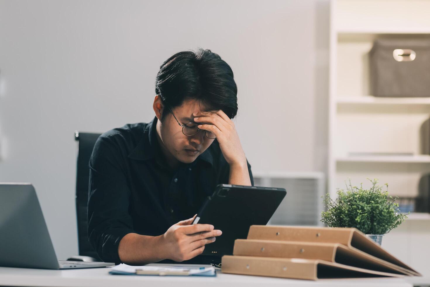 Frustrated Asian young businessman worker working on table in office. Busy employee worker people feel tired and headache from late work and overwork job document on computer desk at company workplace photo