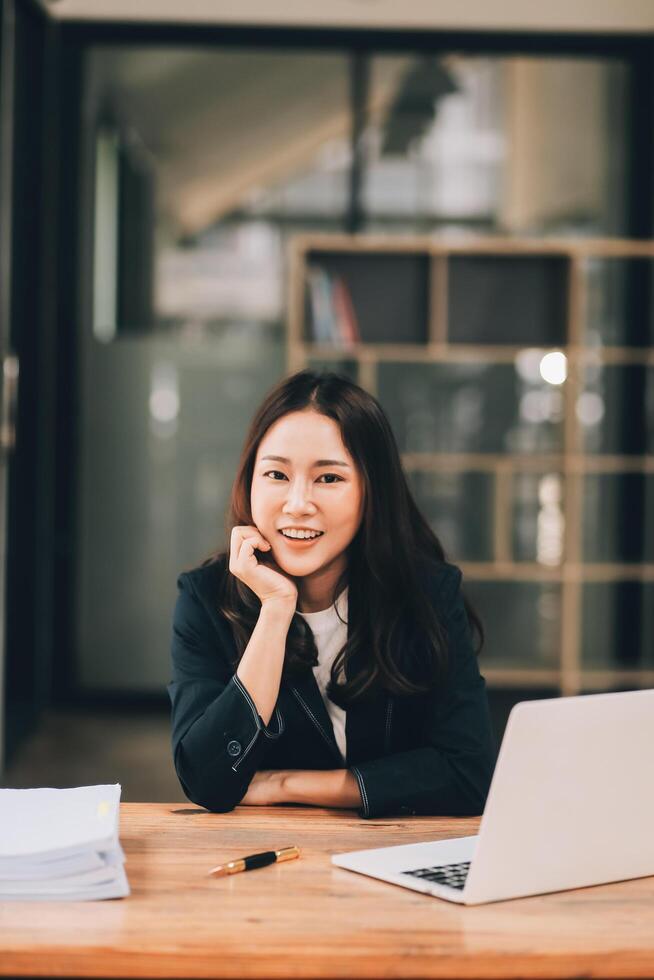 Cheerful business lady working on laptop in office, Asian happy beautiful businesswoman in formal suit work in workplace. Attractive female employee office worker smile. photo