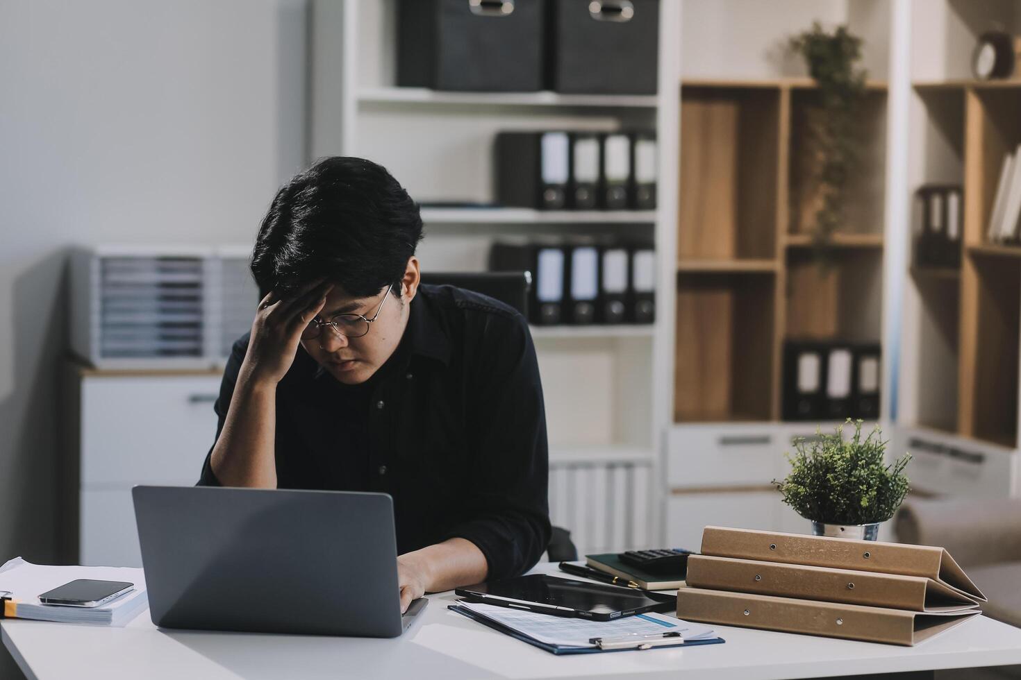 Frustrated Asian young businessman worker working on table in office. Busy employee worker people feel tired and headache from late work and overwork job document on computer desk at company workplace photo