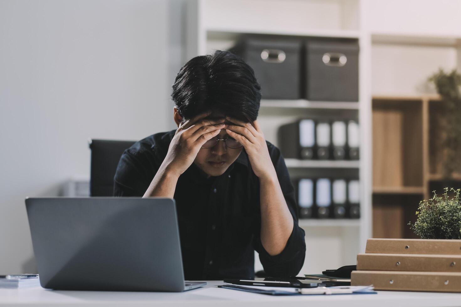 Frustrated Asian young businessman worker working on table in office. Busy employee worker people feel tired and headache from late work and overwork job document on computer desk at company workplace photo