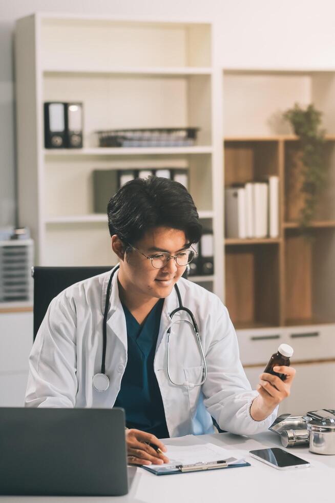 Handsome young doctor with a beard and a lab coat taking of his glasses to read an email in his laptop photo