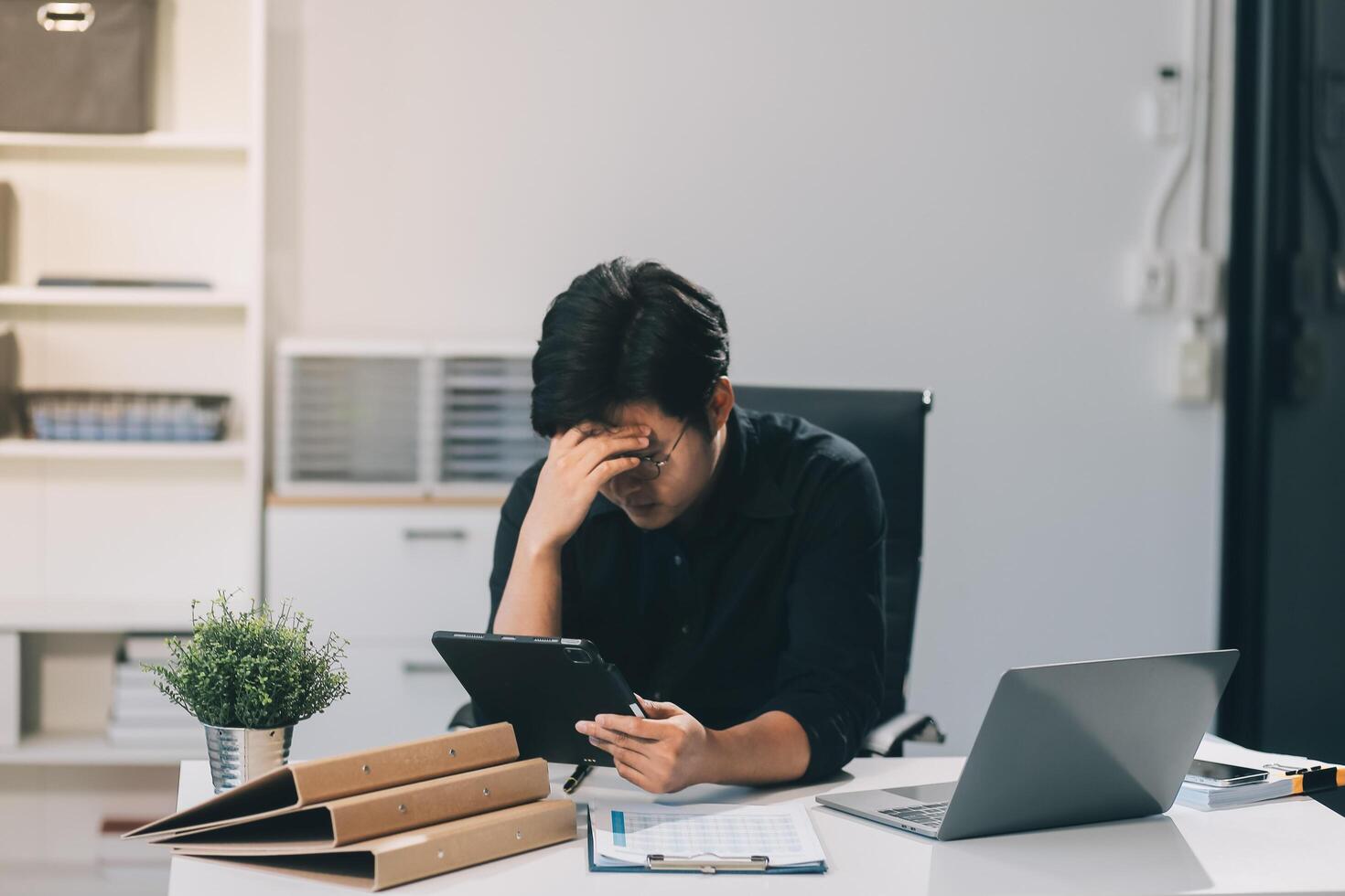 Frustrated Asian young businessman worker working on table in office. Busy employee worker people feel tired and headache from late work and overwork job document on computer desk at company workplace photo