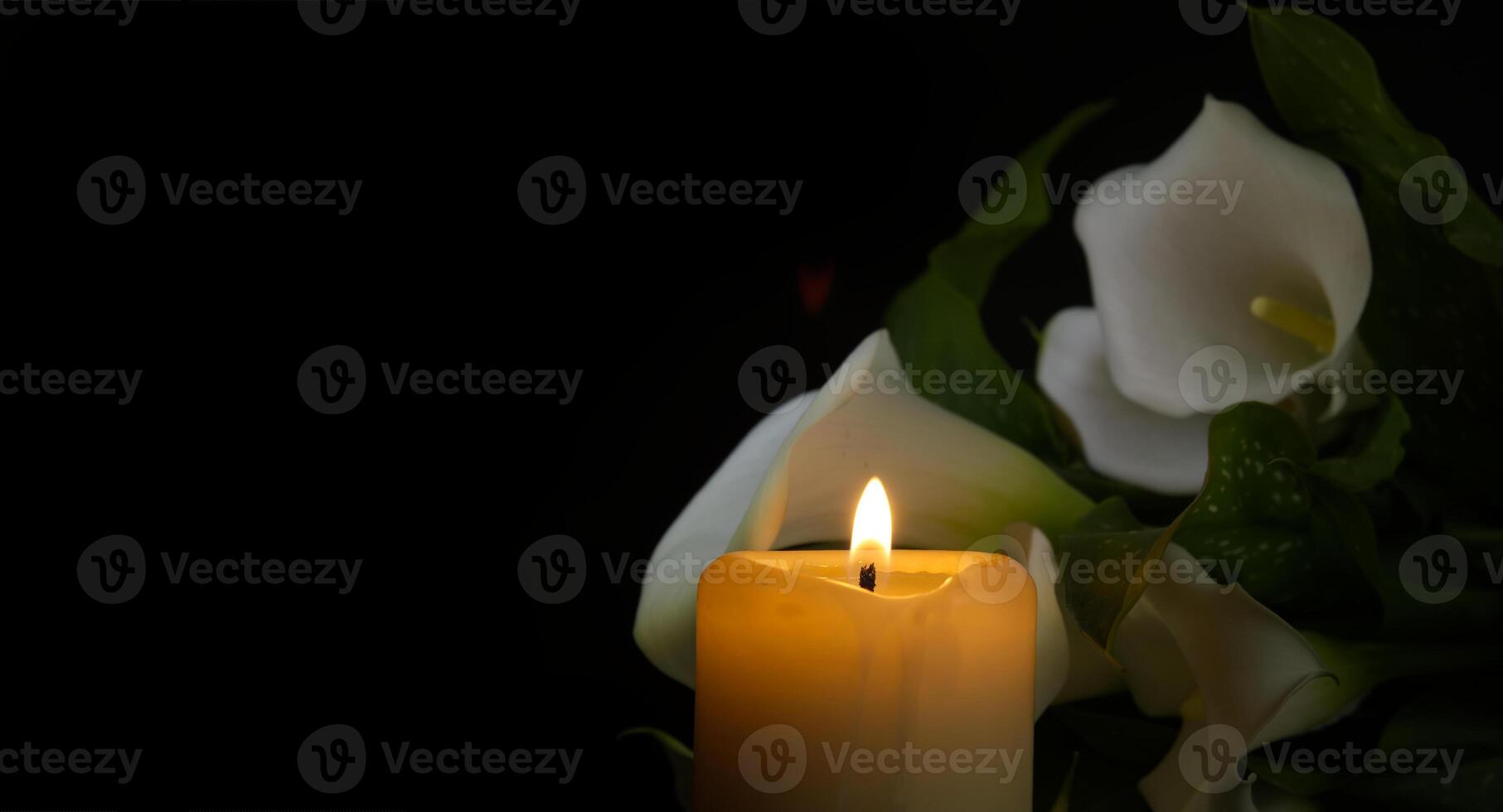 Burning wax candle and white calla lily flowers in darkness photo