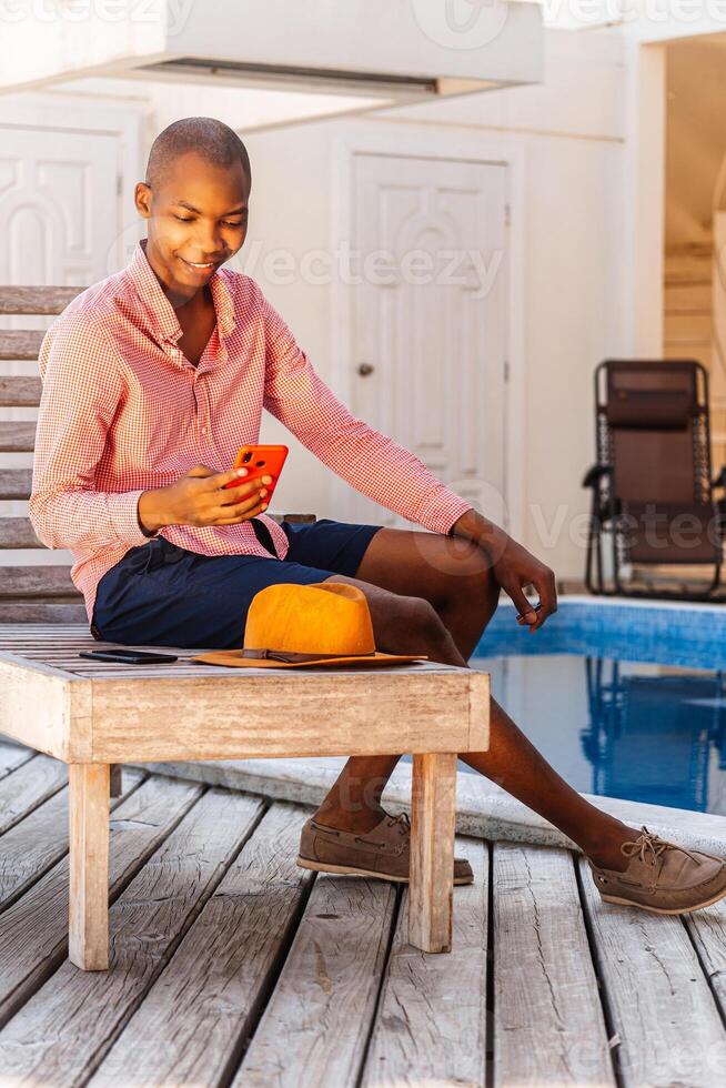 Black african young man using a smartphone behind a pool. photo