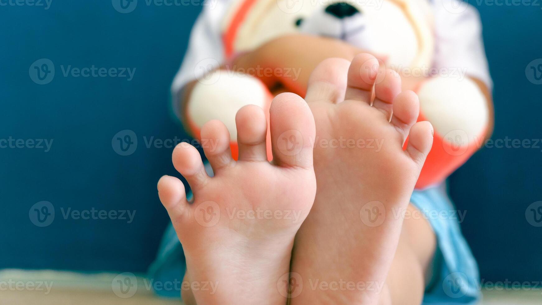 Asian young girl sitting on the floor, hugging the white doll. Closeup the bare feet. photo