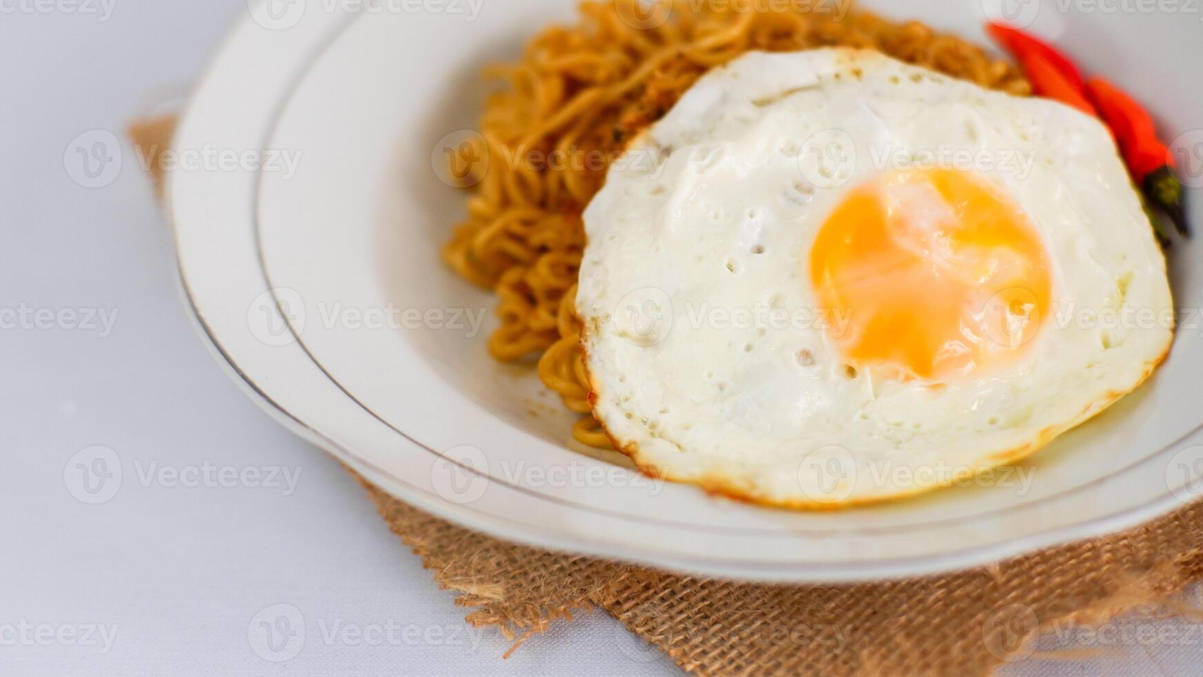 Fried noodles with fried egg and red cayenne pepper. Served on a serving white plate. Isolated on white background. photo
