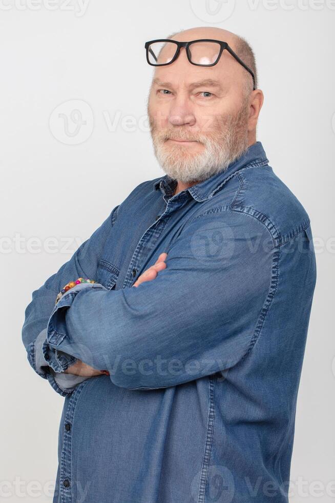 Portrait of an attractive gray-haired man with glasses wearing a denim shirt isolated on a gray background. Bearded grandfather of the European type. photo